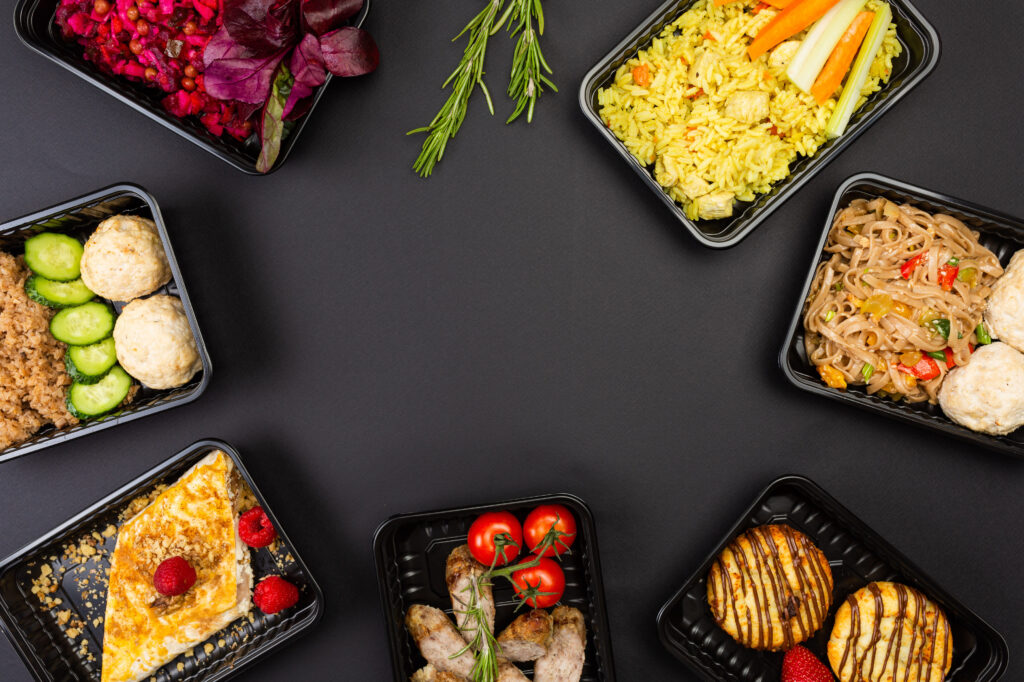 Ready healthy food catering menu in lunch boxes meat and vegetable packages as daily meal diet plan courier delivery with fork isolated on black table background. Top view. Free space for your text.
